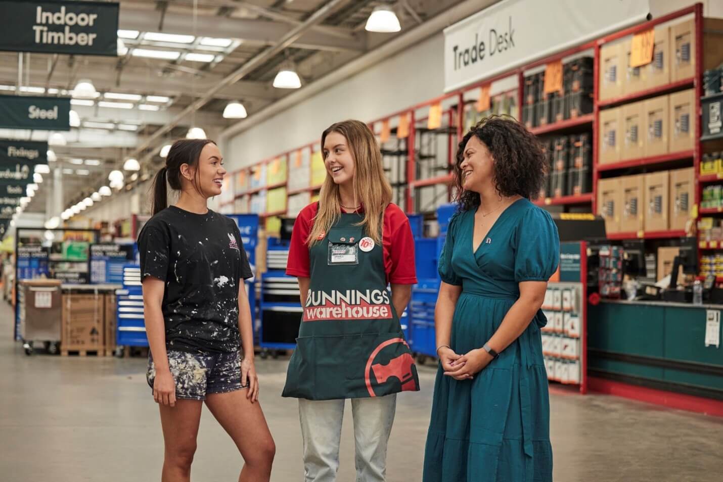 Female tradeswoman, female Bunnings employee and Lisa Martello from the NAWIC Diversity & Inclusion Portfolio standing inside a Bunnings store talking and smiling amongst each other.